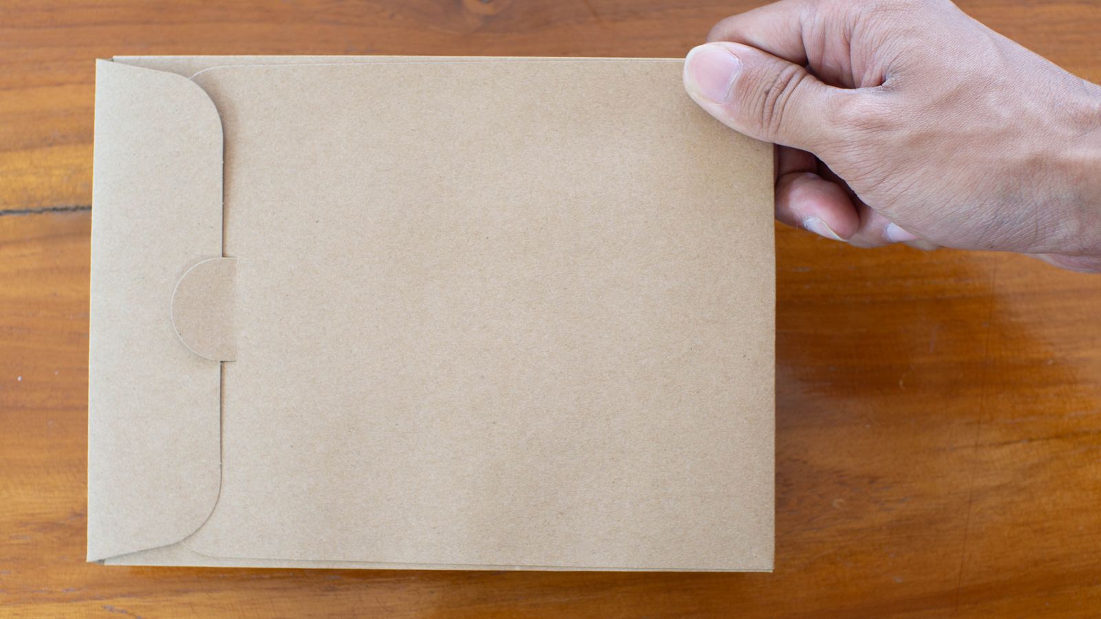 Photograph of a hand holding an unopened arrears letter in a brown envelope