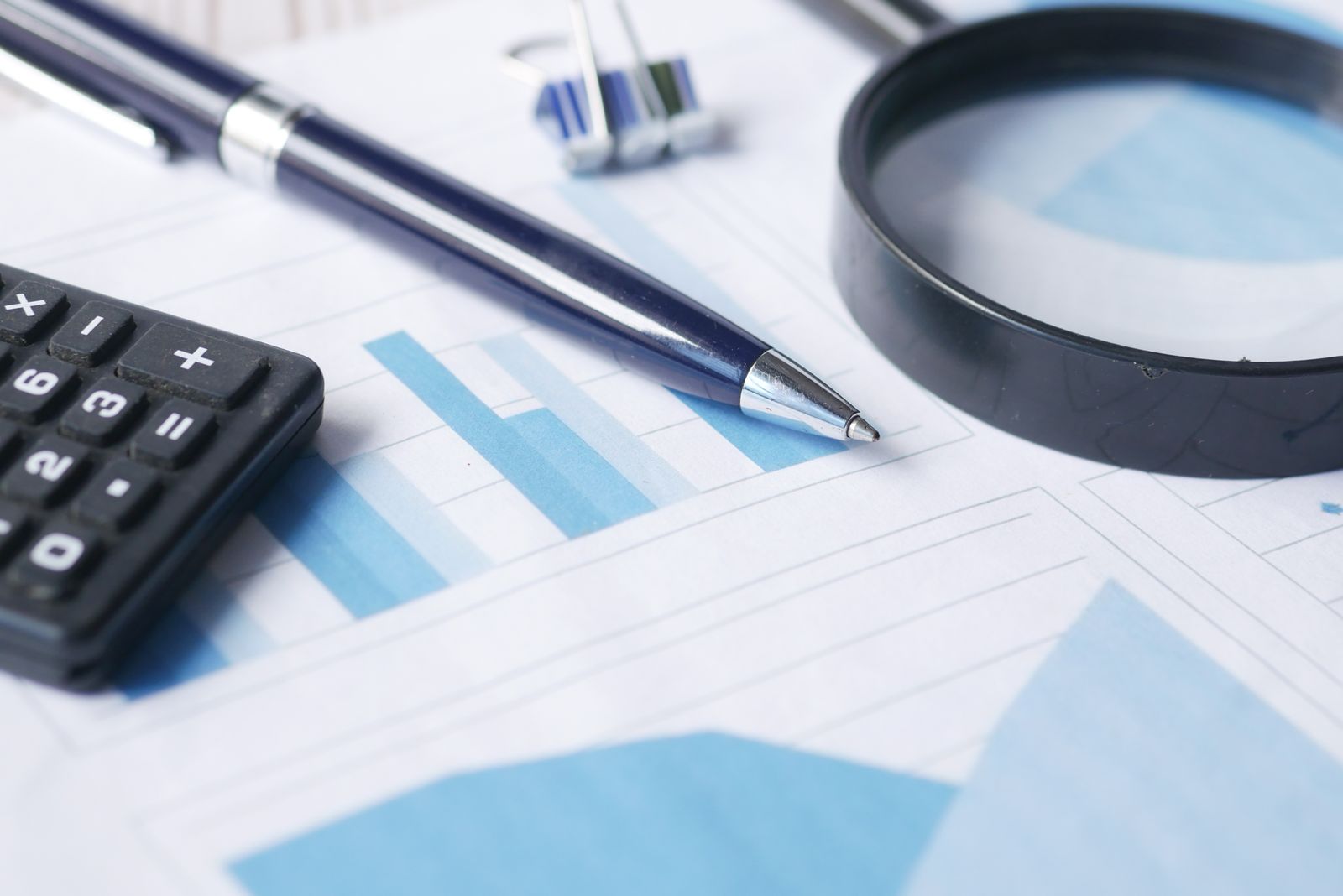Photograph of financial documents under review with a calculator and magnifying glass during audit preparation