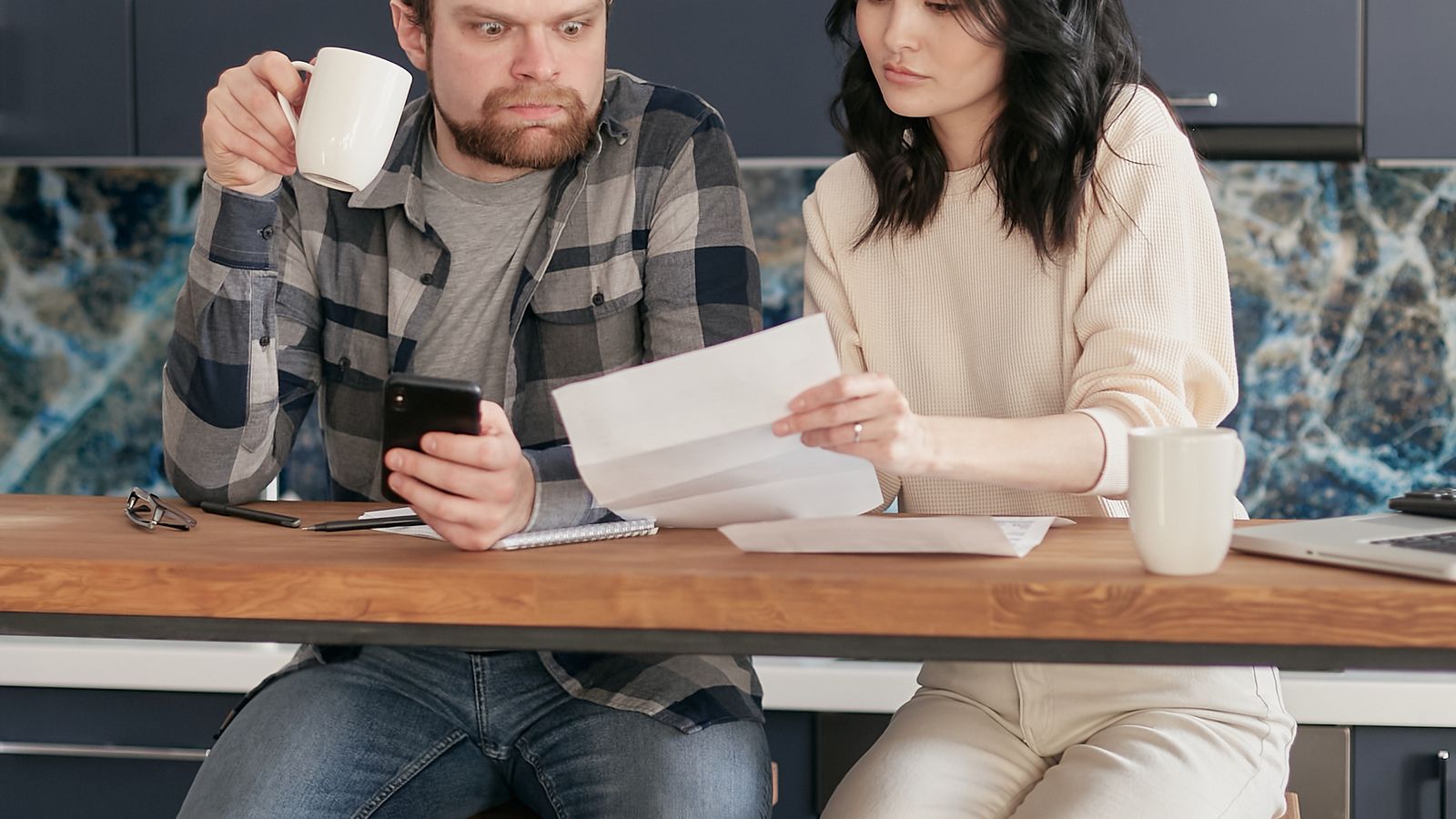 Photograph of a worried couple reviewing bills and school fees at their kitchen table